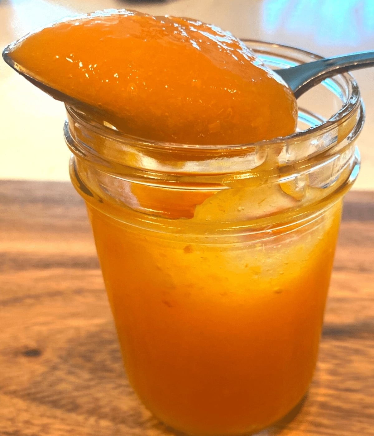 apricot freezer jam in half pint mason jar with a spoon ful of golden apricot freezer jam on top