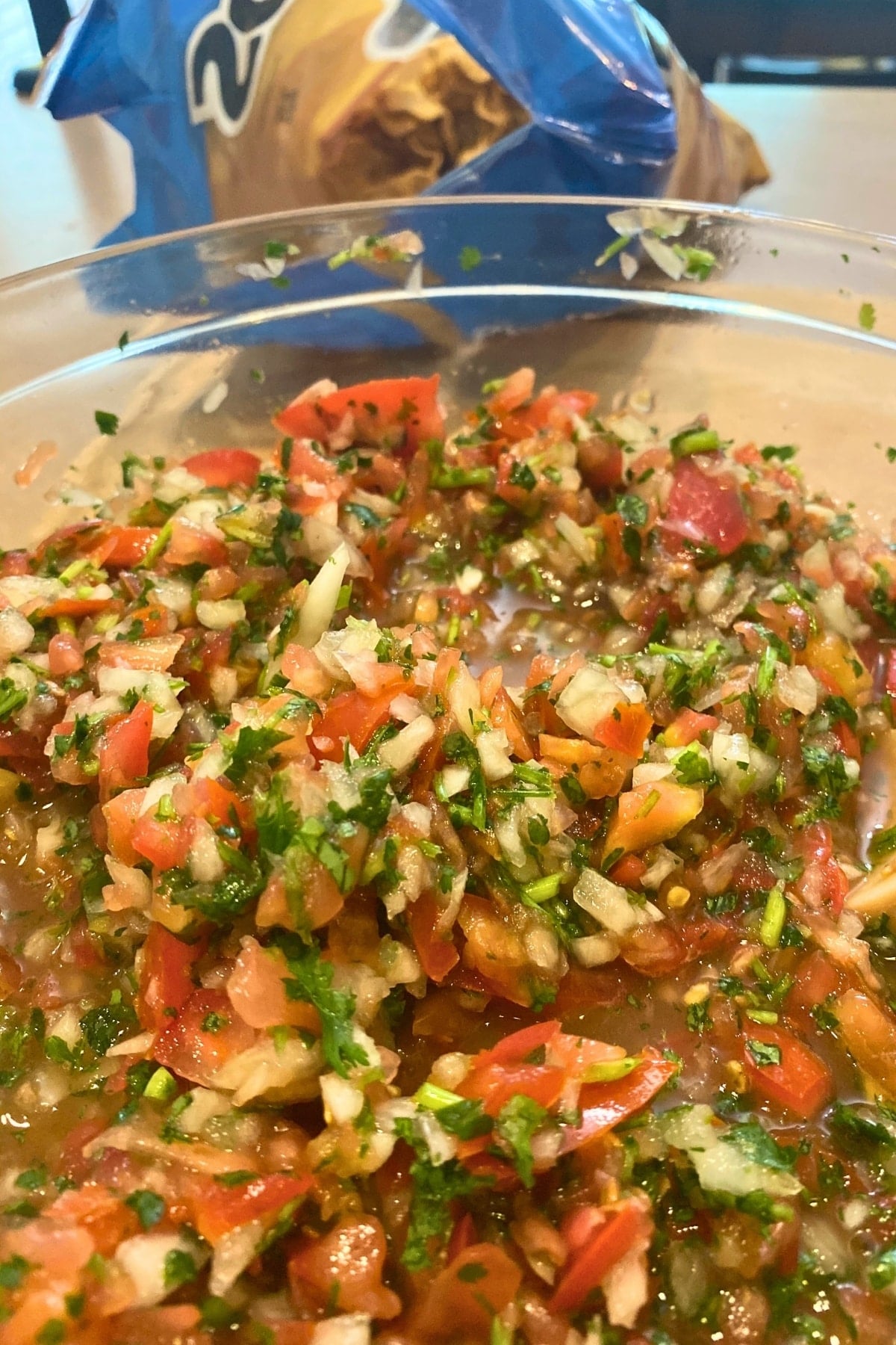 pico de galllo in a glass bowl with a bag of tortilla chips in the background