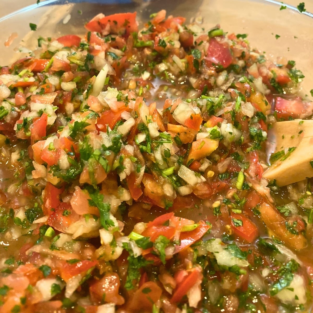 pico de gallo in a glass bowl with a wooden spoon