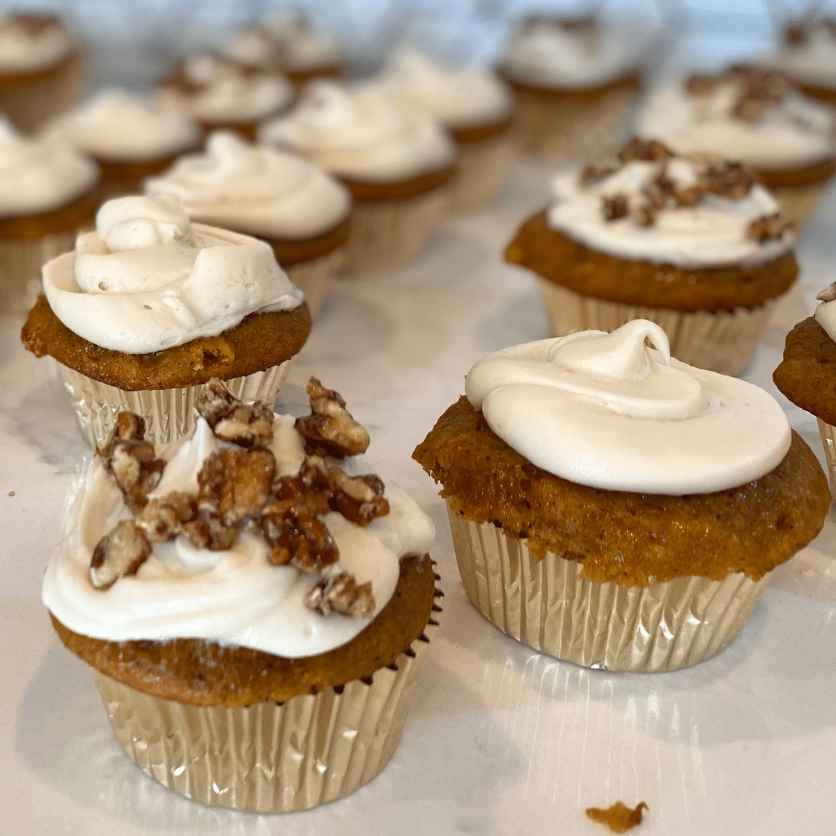 pumpkin cupcakes with cream cheese frosting and candied pecans on counter top
