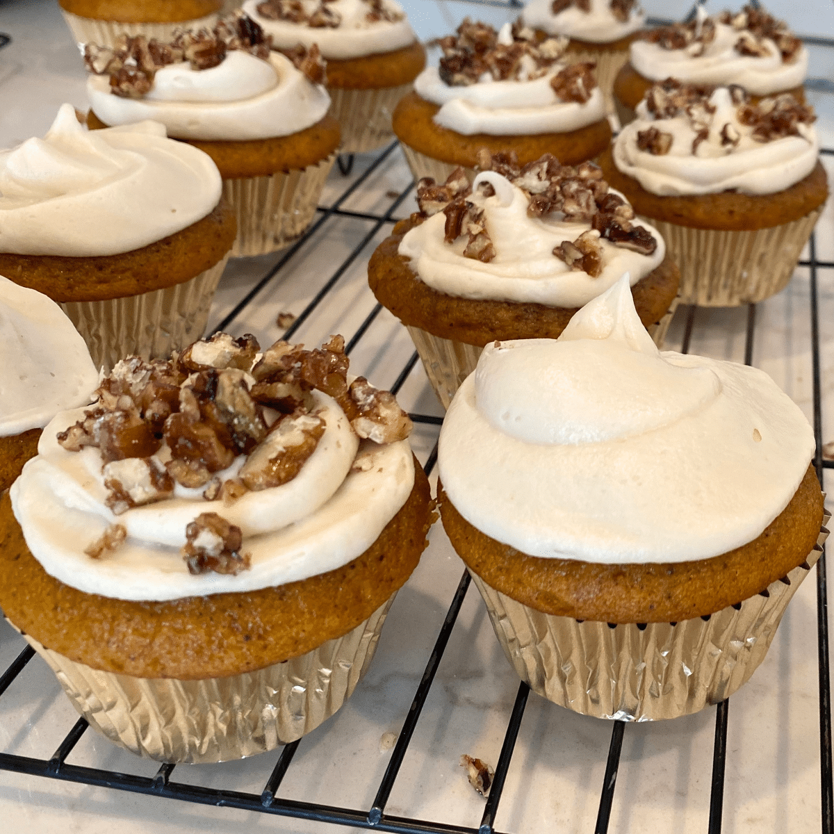 pumpkin cupcakes with cream cheese frosting and candied pecans cooling on wire rack