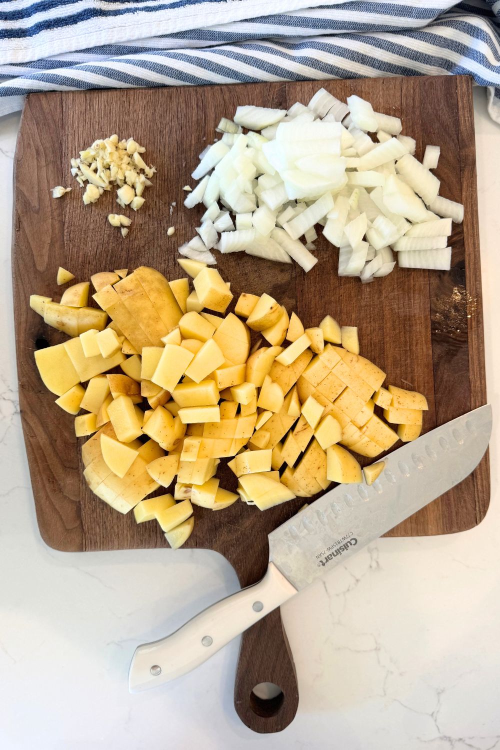 chopped potatoes, onion and minced garlic on cutting board with knife