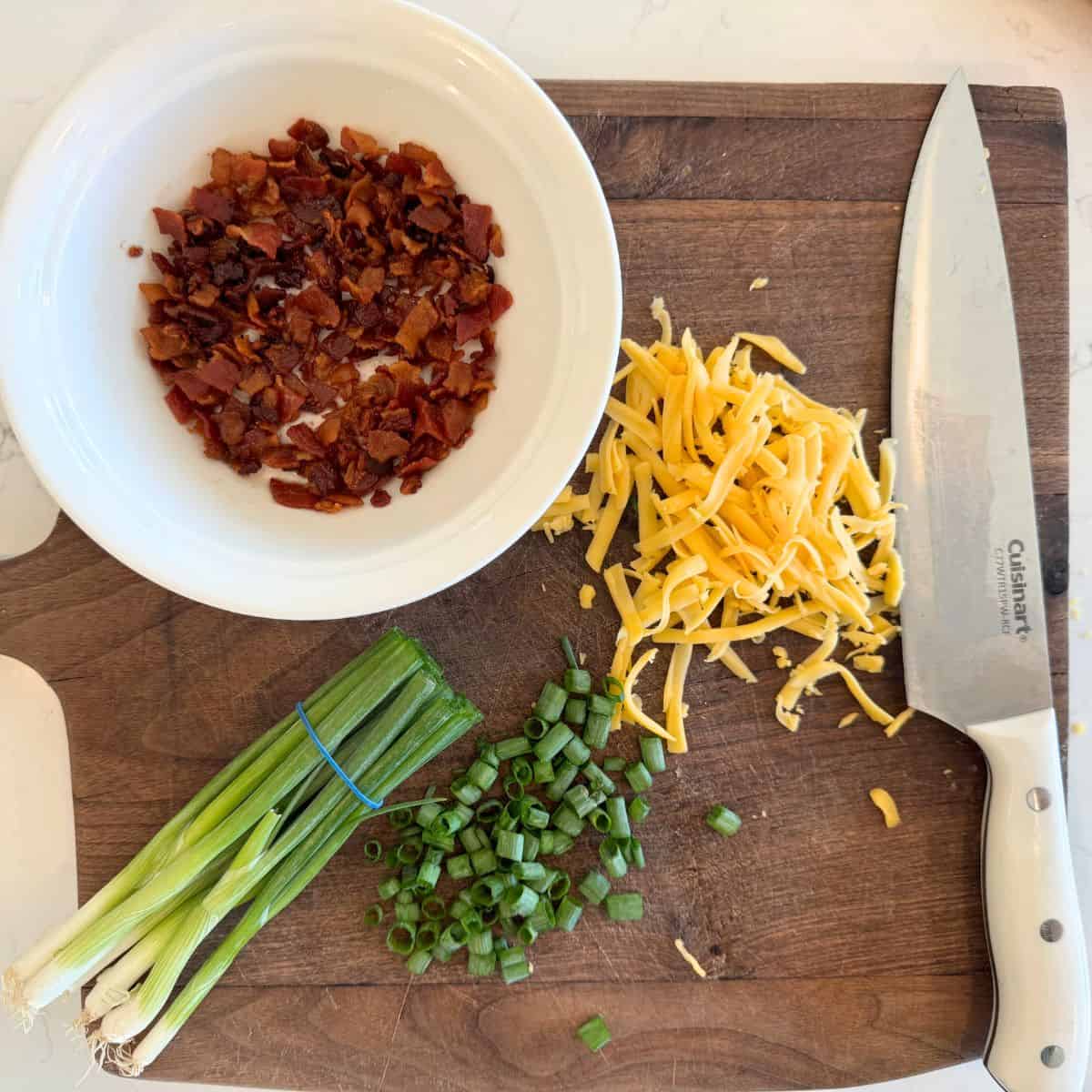 potato soup toppings crisp backon pieces, chopped green onions and shredded cheddar cheese on a cutting board with a knife