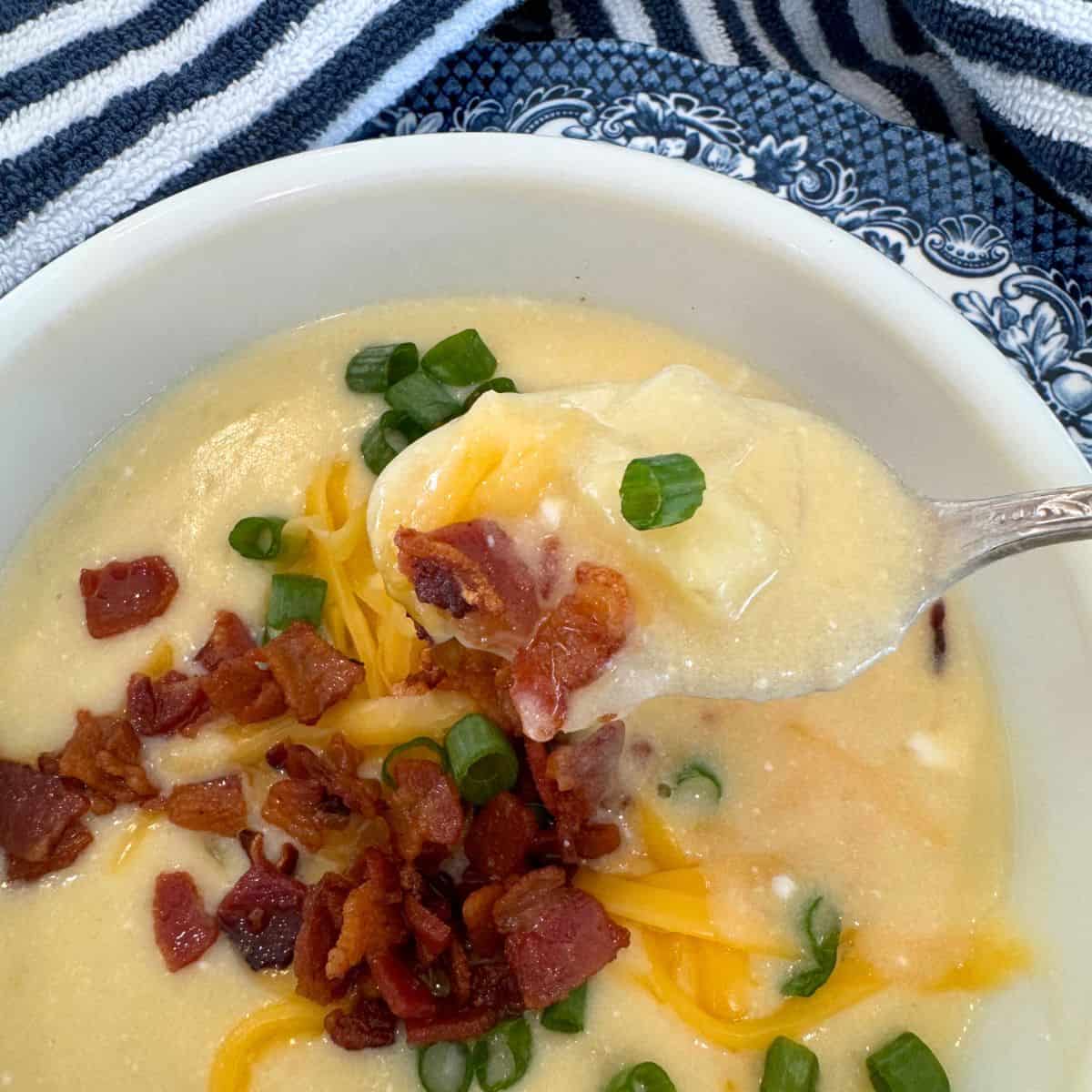 the best crock pot potato soup recipe dished out in a bowl garnished with crisp bacon, green onions and cheddar cheese.