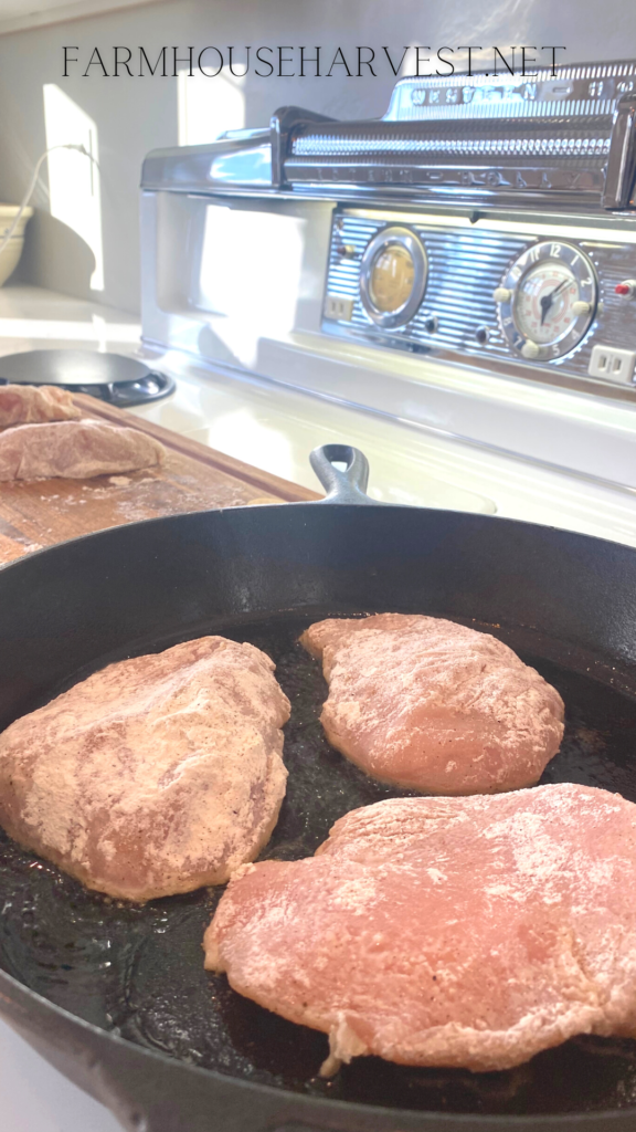 seasoned dredged and browning chicken breasts in a cast iron skillet on the stove top.