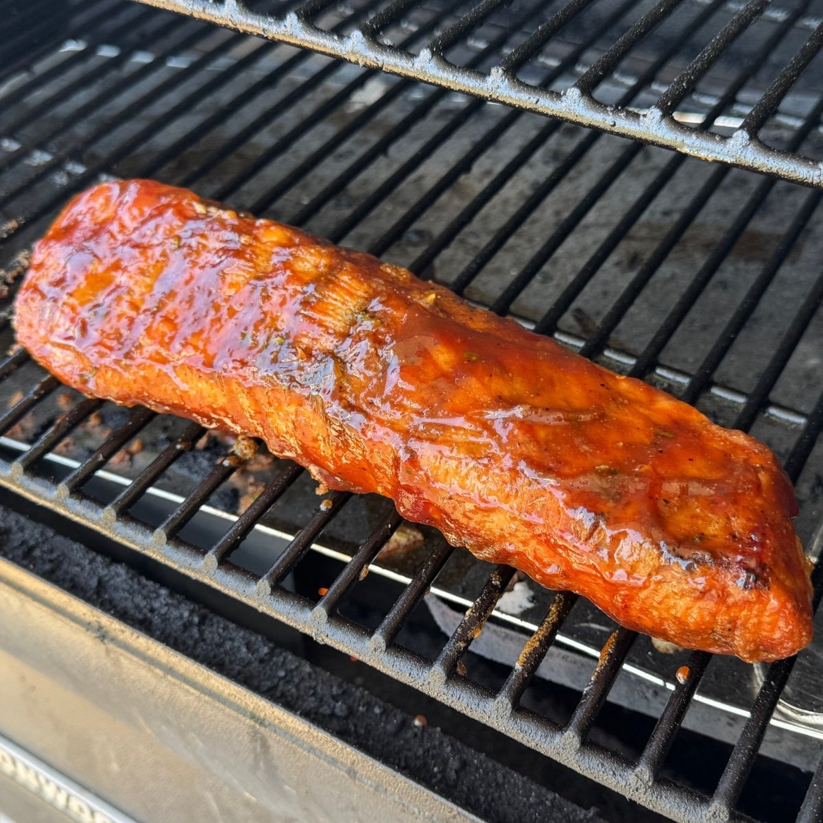 grilled pork tenderloin brushed with BBQ sauce on grill