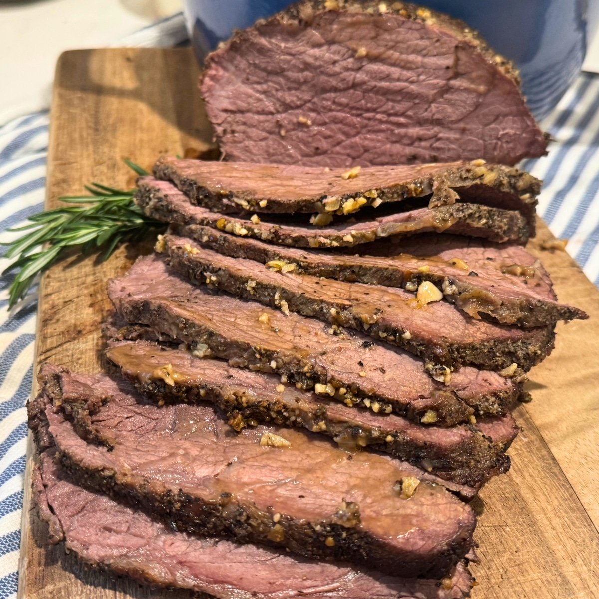 sliced rump roast on cutting board with a sprig of rosemary