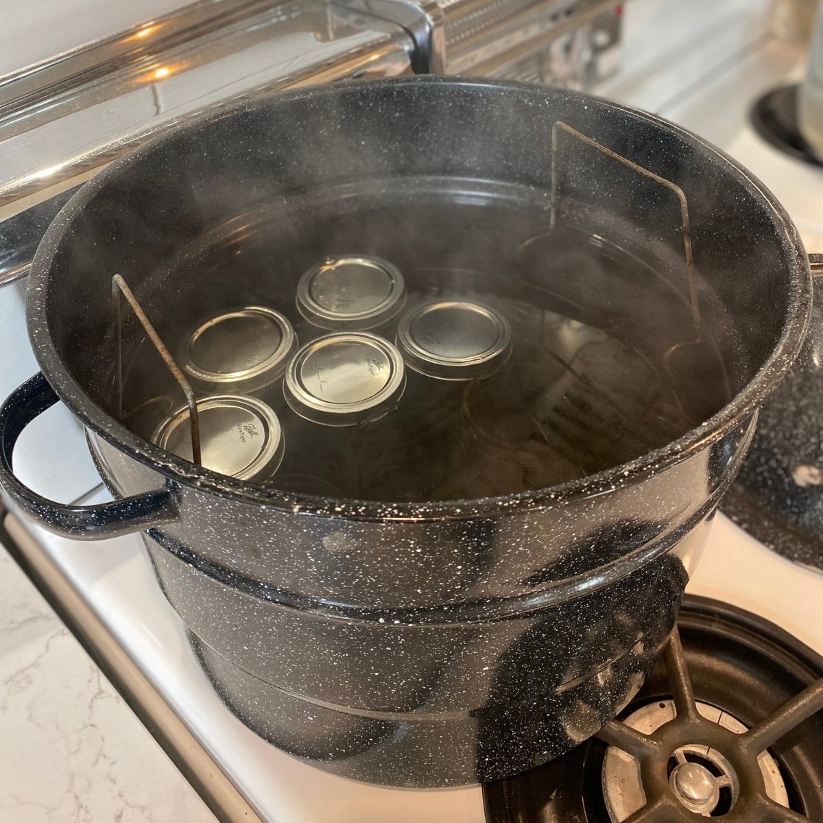 water bath canner with jar rack, jars, and hot water on stove