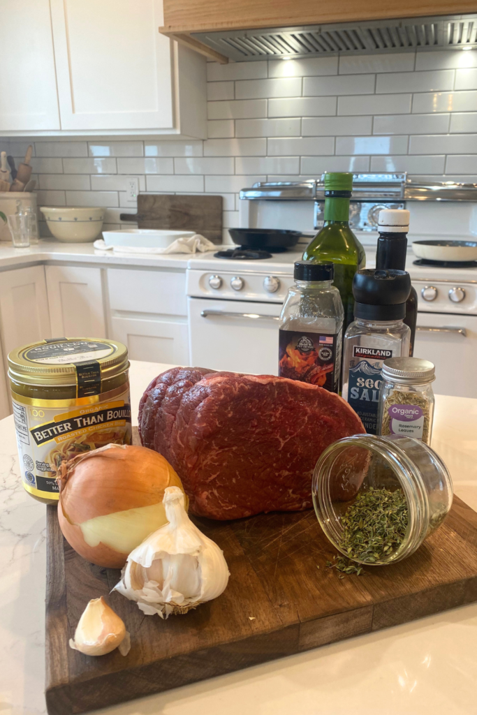 ingredients: rump roast, broth, onion, garlic, thyme; rosemary, salt, pepper, oil and Worcestershire sauce all on cutting board