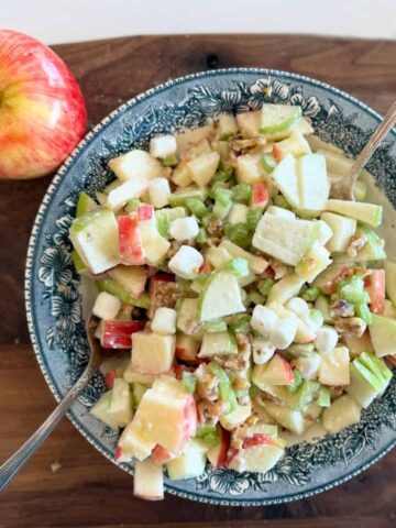 Waldorf apple salad with mini marshmallows on blue bowl on cutting board with apple on the side