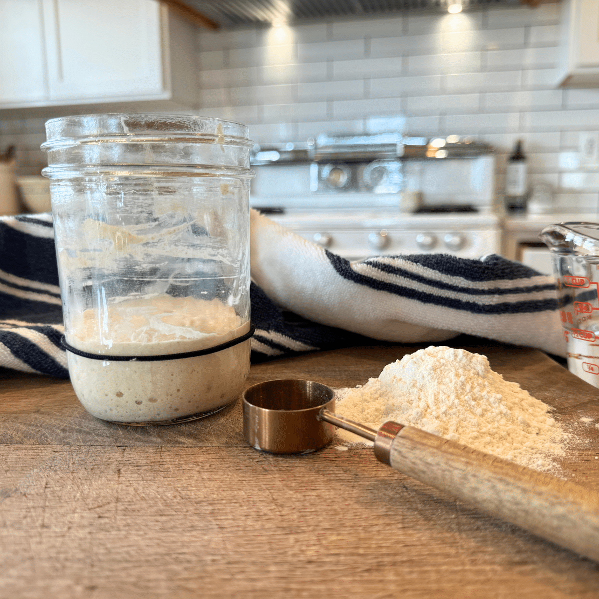 activating sourdough starter in jar with tablespoon and flour on cutting board