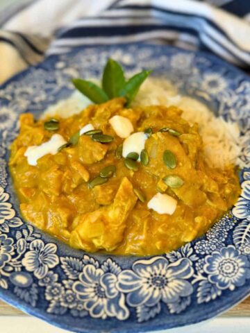 pumpkin chicken currey garnished with pumpkin seeds and heavy cream served with rice on blue plate.