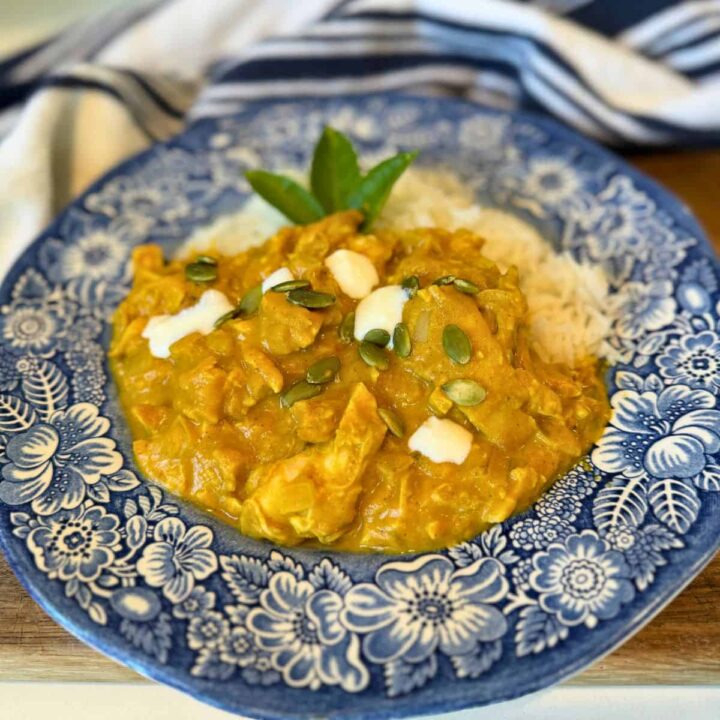 pumpkin chicken currey garnished with pumpkin seeds and heavy cream served with rice on blue plate.