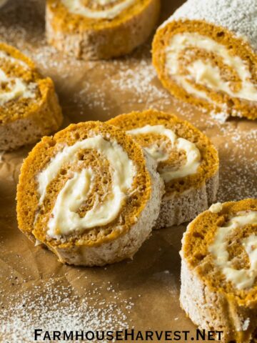 pumpkin roll sliced on parchment paper dusted with powdered sugar with the text FarmhouseHarvest.net