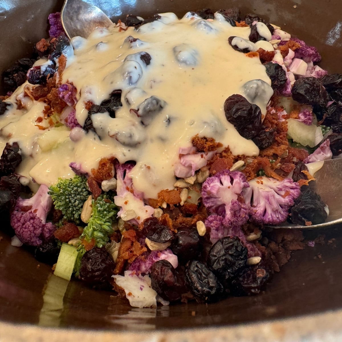 all chopped bacon broccoli salad ingreidnets in bowl covered with the homemade dressing and spoons ready to stir