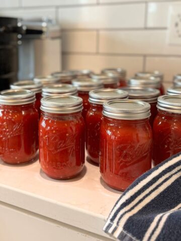 20 pints of home canned crushed tomatoes in jars on counter with water bath canner behind them.