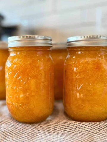 low sugar peach jam canning recipe in jars on cloth on counter