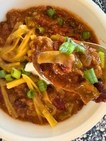 a bowl of crockpot chili garnished with cheese and a spoonful to show texture