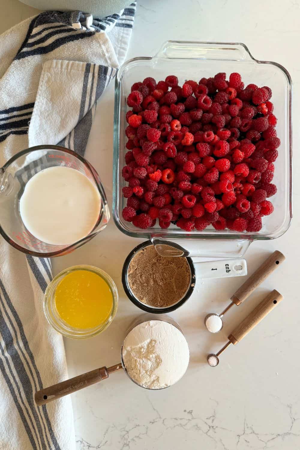 raspberry cobbler ingredients measured out on counter: raspberries, flour, sugar, milk, melted butter, baking powder, salt and sugar