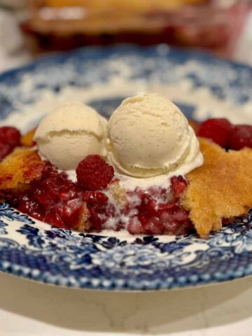 raspberry cobbler with a scoop of vanilla ice cream on top on a blue plate