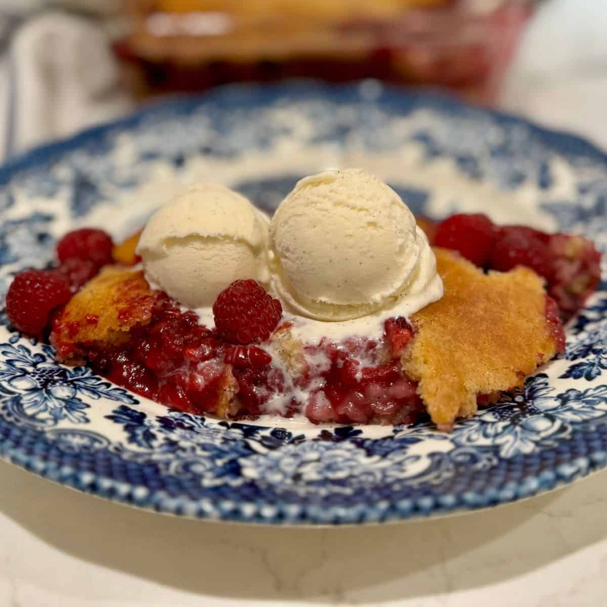 raspberry cobbler with a scoop of vanilla ice cream on top on a blue plate