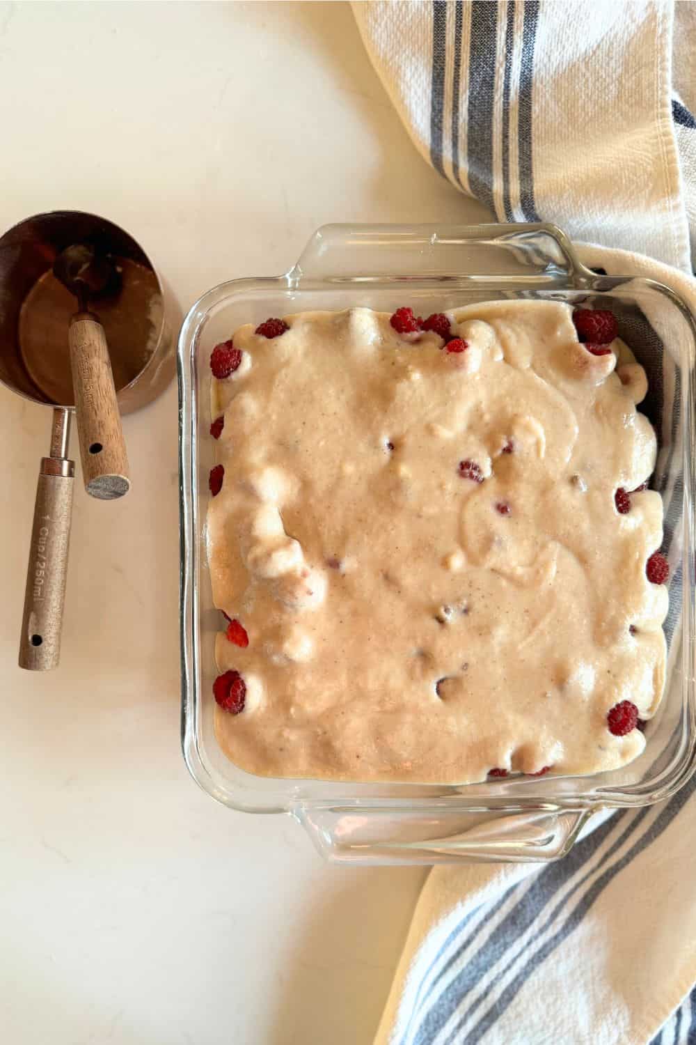 raw batter poured over the raspberries in the baking dish on the counter