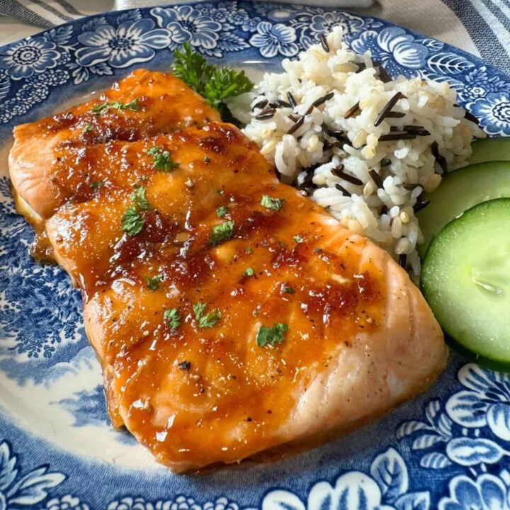 Baked Glazed Salmon served on a blue plate with chopped parsley, wild rice pilaf and cucumber slices.