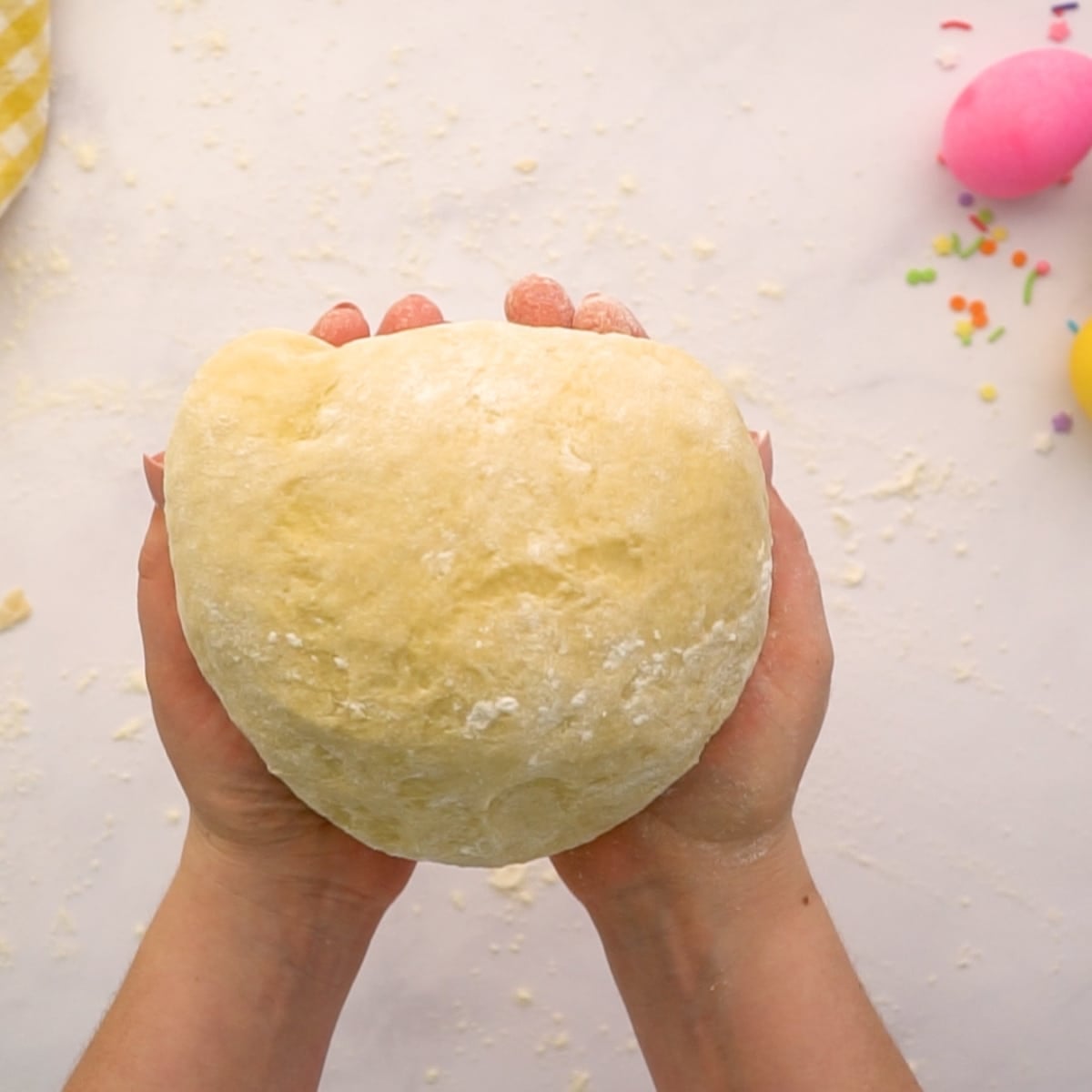 sourdough easter bread dough ball in hands ready to roll and braid with easter eggs and sprinkles on the tabel in the upper corner