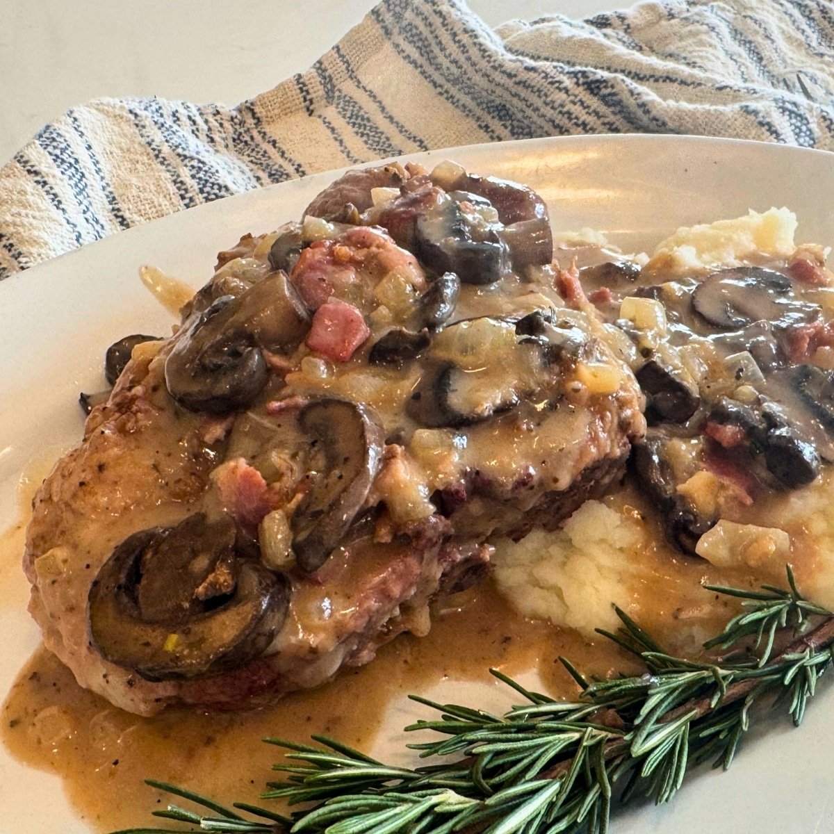 smothered pork chop served over mashed potatoes garnished with rosemary sprig