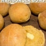 A close-up shot of freshly baked golden brown sourdough hamburger buns resting on a wire cooling rack. The buns have a perfectly smooth, rounded shape with glossy tops brushed with melted butter and sprinkled with sesame seeds, showcasing a soft, fluffy texture.