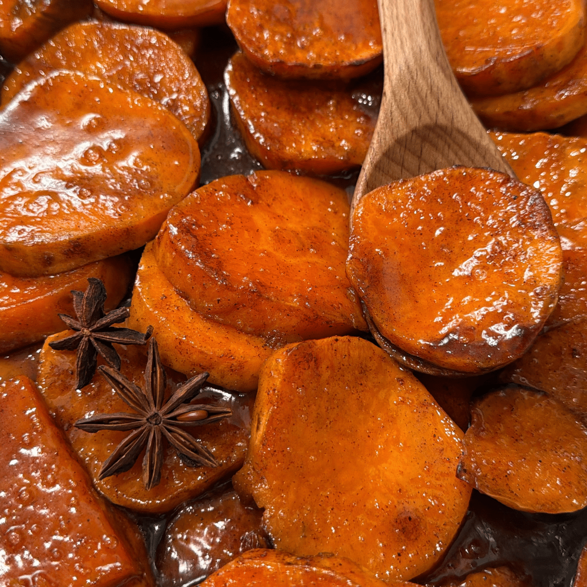 baked candied yams in caramel sauce in baking dish with wooden spoon