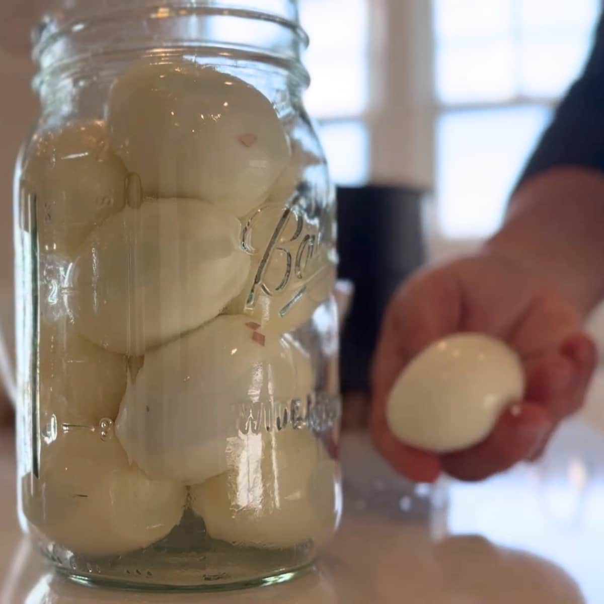 easy peeled egg in hand by egg jar with the instant pot insert in background