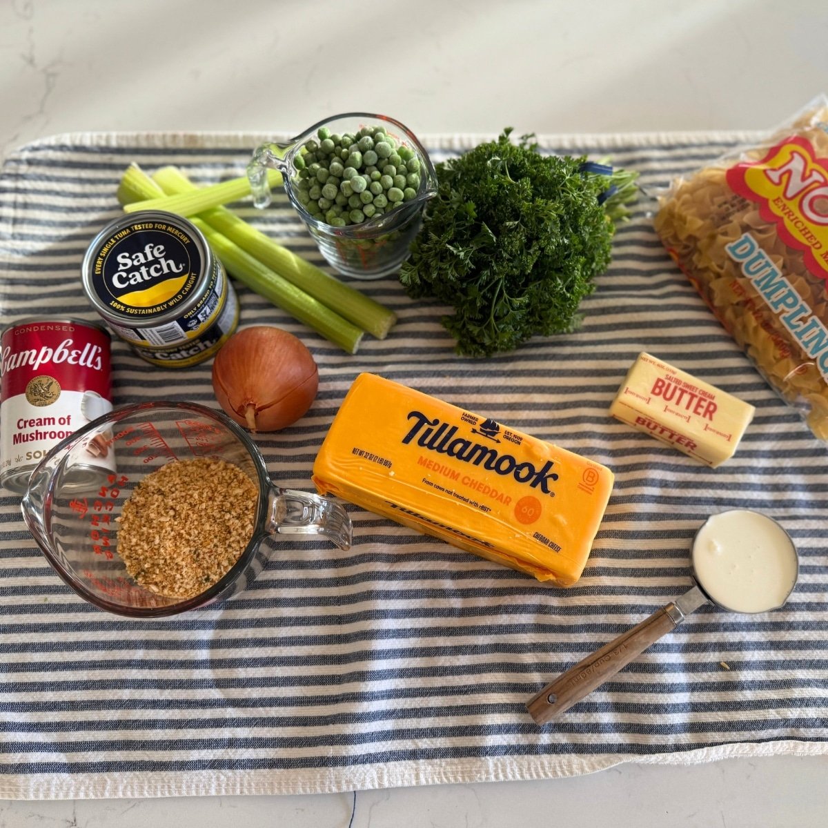 tuna casserole ingredients cream of mushroom soup, 2 cans tuna, italian panko crumbs, cheese, onion, celery, frozen peas, butter, cream and egg noodles, and fresh parsley