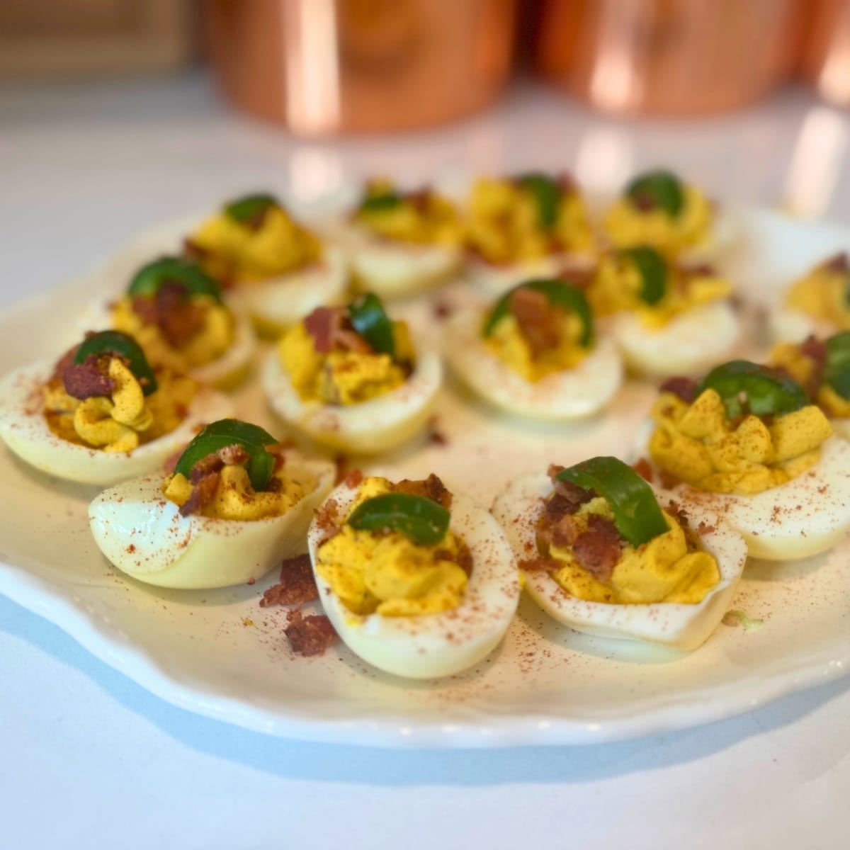 Close-up of farmhouse-style deviled eggs topped with bacon and jalapeños on a serving plate.