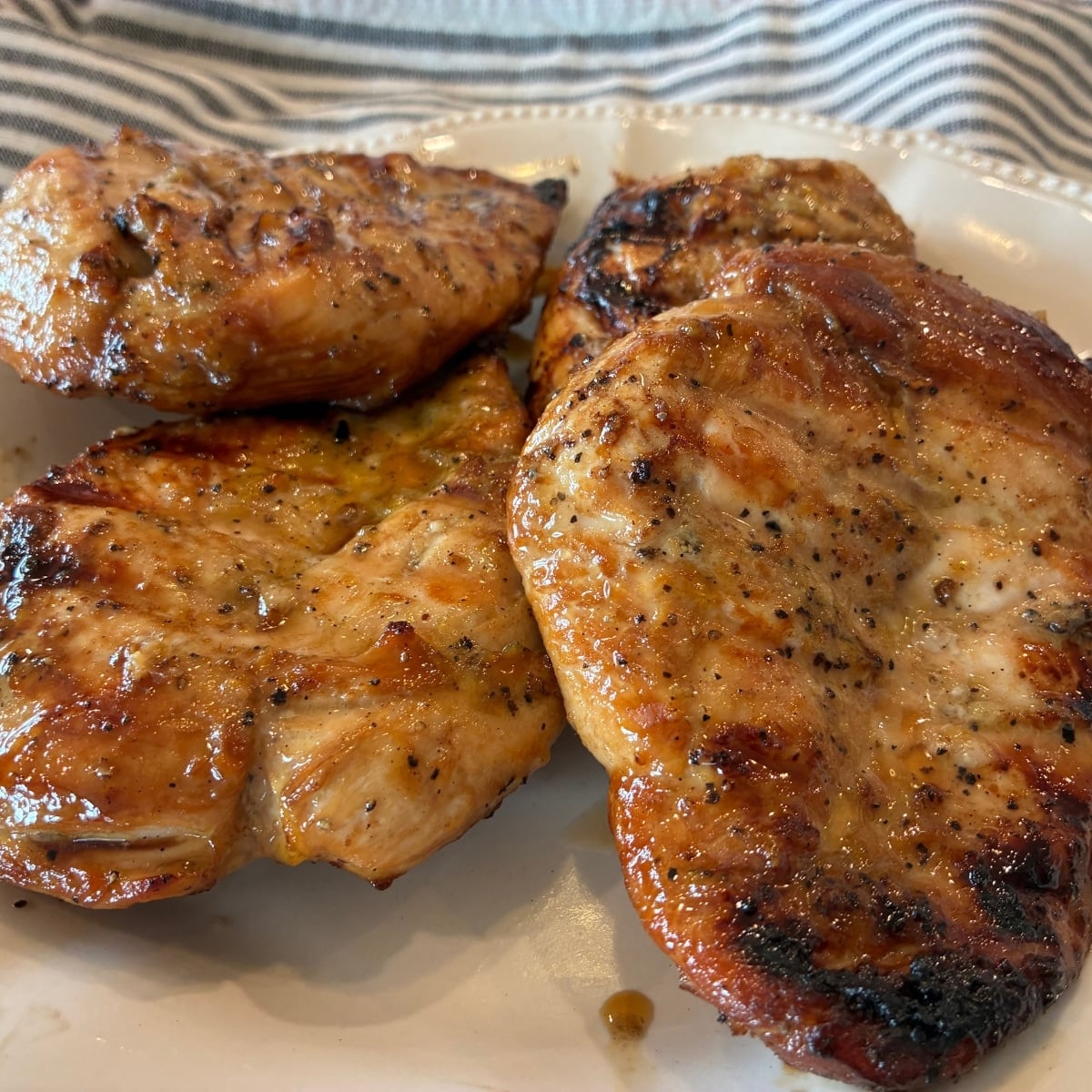 lemon garlic grilled chicken on plate after grilling showing pepper and grill marks, with kitchen towel in background