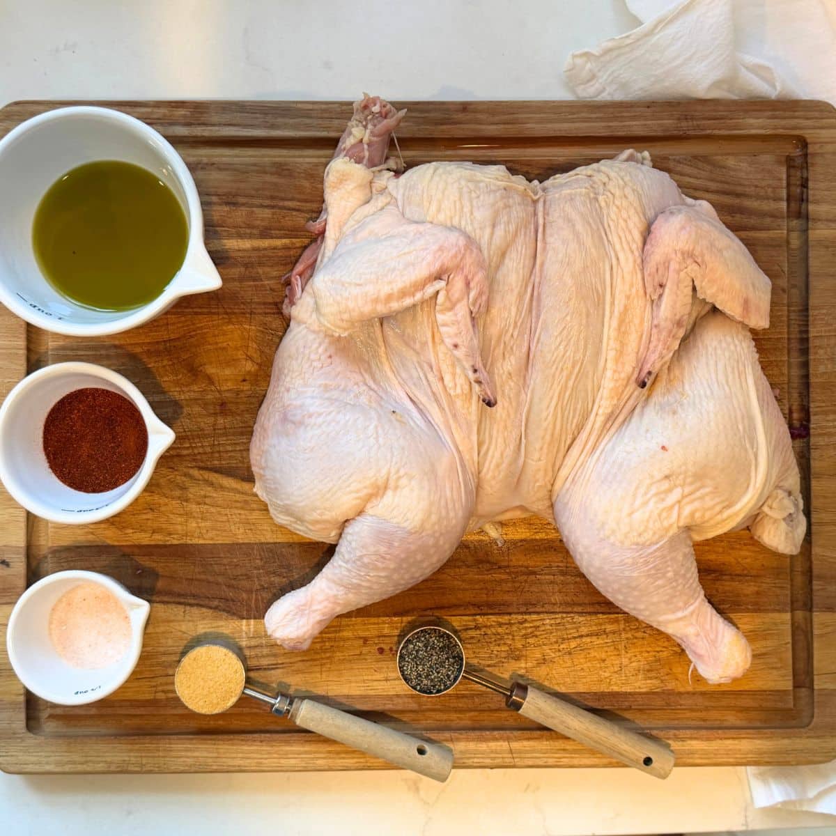 raw chicken resting on cuting board with cups containing olive oil, smoked paprika, salt pepper and garlic powder