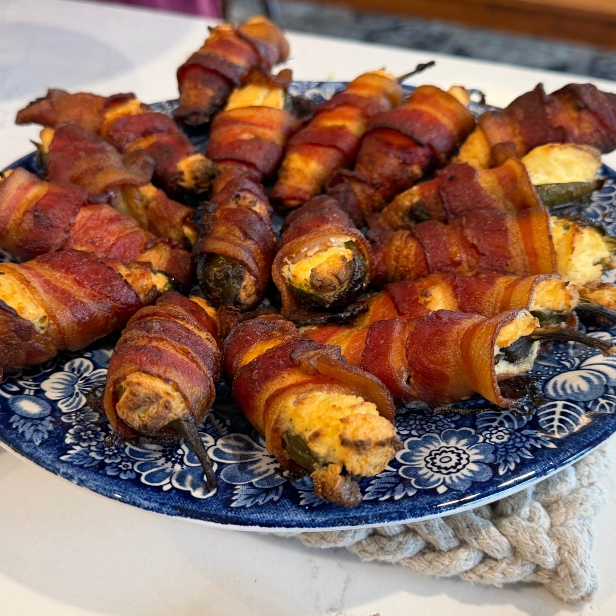 side view Grilled Bacon Wrapped Stuffed Jalape&ntilde;os on blue serving plate