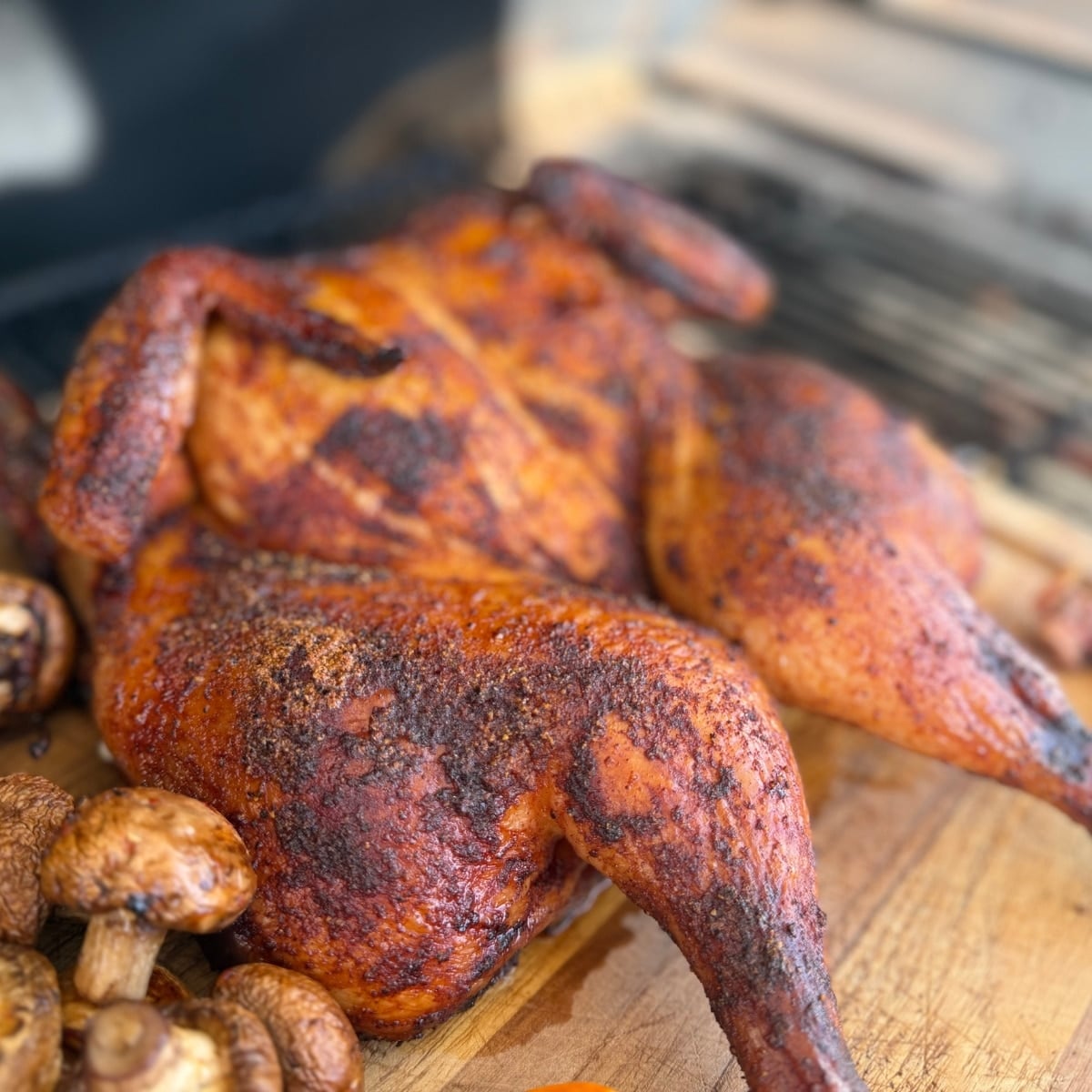 Whole spatchcocked chicken grilled to a golden brown with smoked paprika rub, resting on a wooden farmhouse cutting board with grilled muchrooms