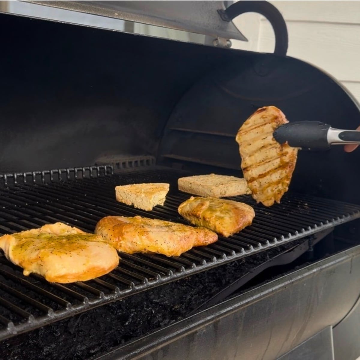 turning chicken breast over on the grill showing grill marks on chicken breast
