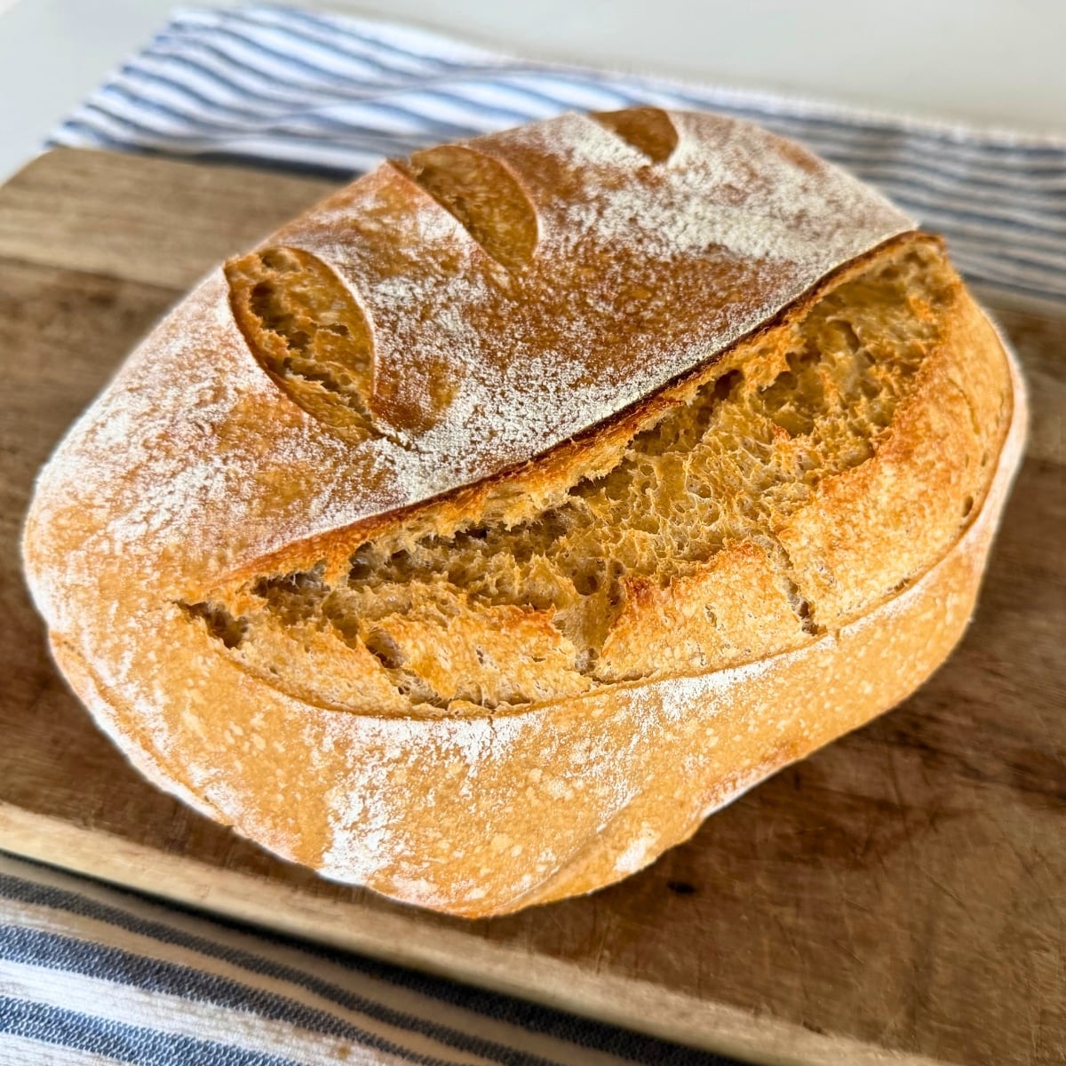 a golden brown loaf of whole wheat sourdough bread cooling on cutting board