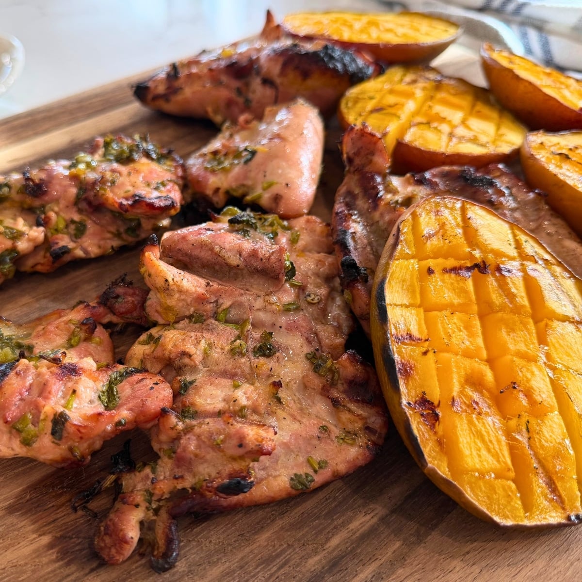Citrus-Marinated Grilled Chicken Thighs with Grilled Mangoes on a wood cutting board