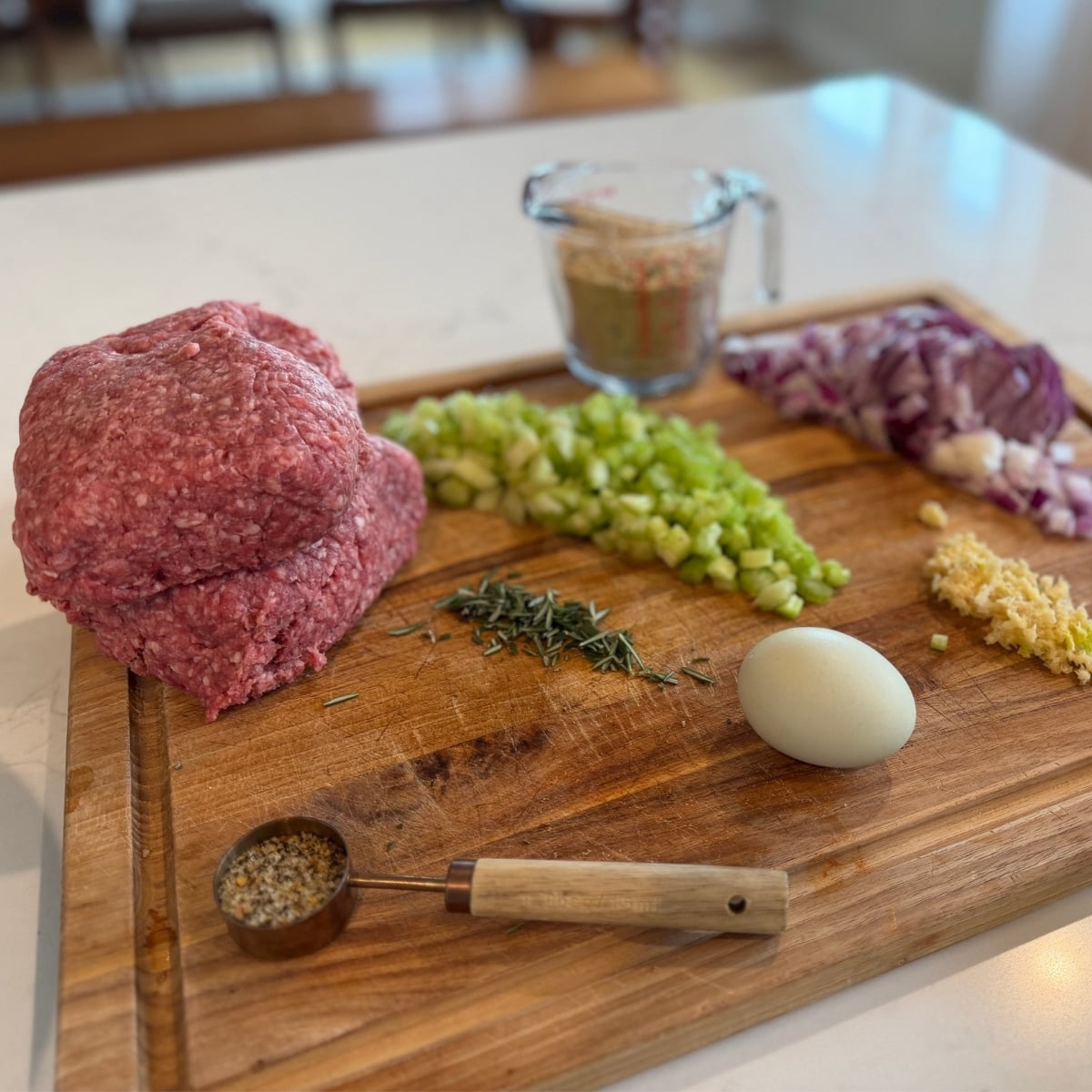 Easy Grilled Meatloaf ingredients on cutting board 2 lbs ground beef, egg, steak seasoning, roasemary, celery, onion, garlic, italian bread crumbs