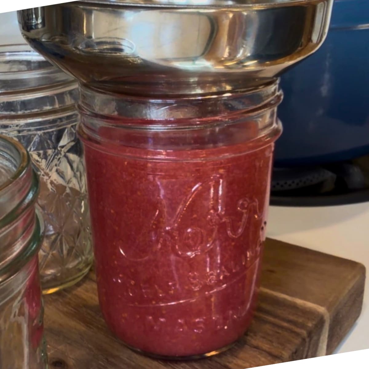 Filling half pint jars with hot low sugar straberry jam canning recipe using a finney and a ladle. Filling to leave 14 an inch headspace