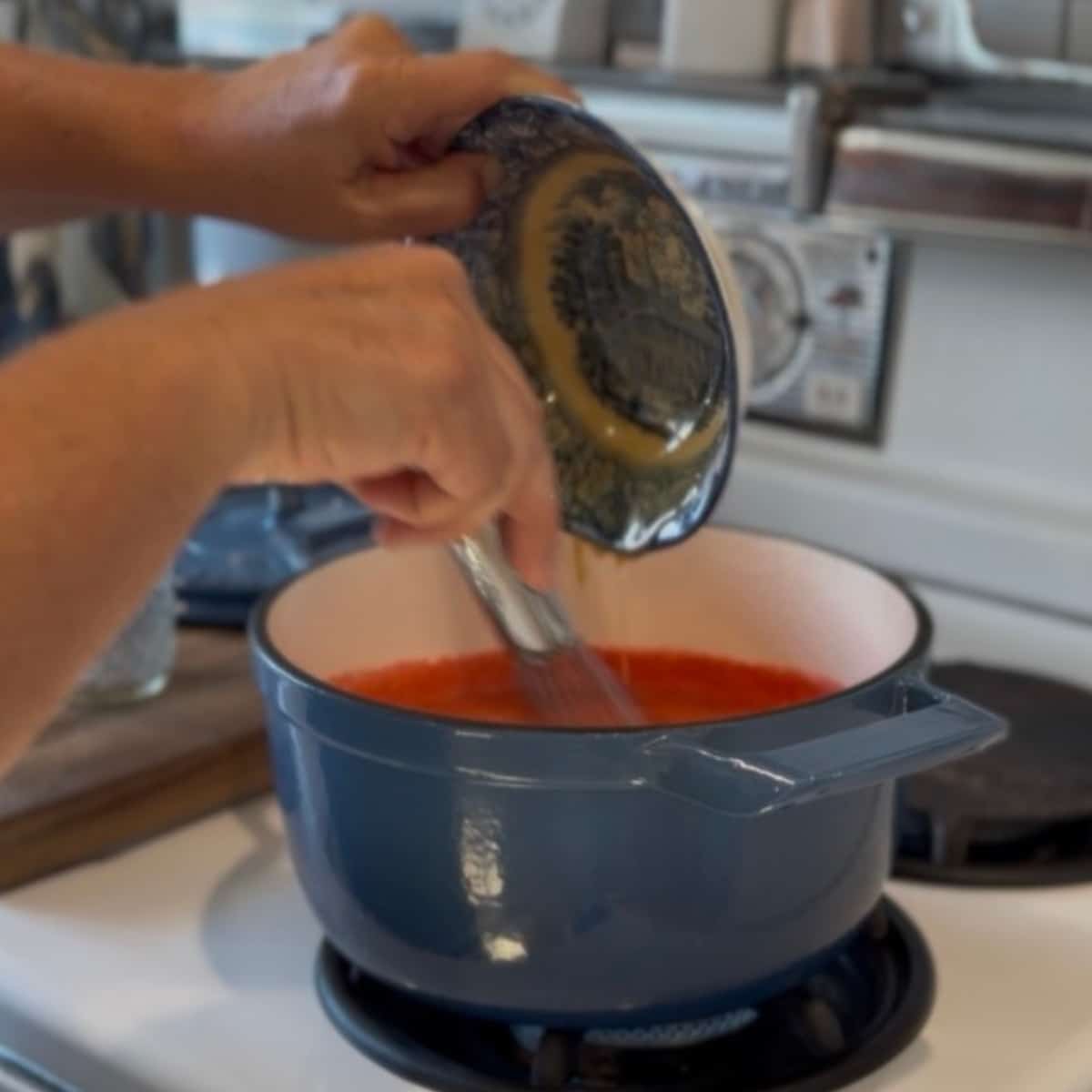 adding honey with pectin powder in it into the pot of boiling strawberry puree and whisking in with a whisk