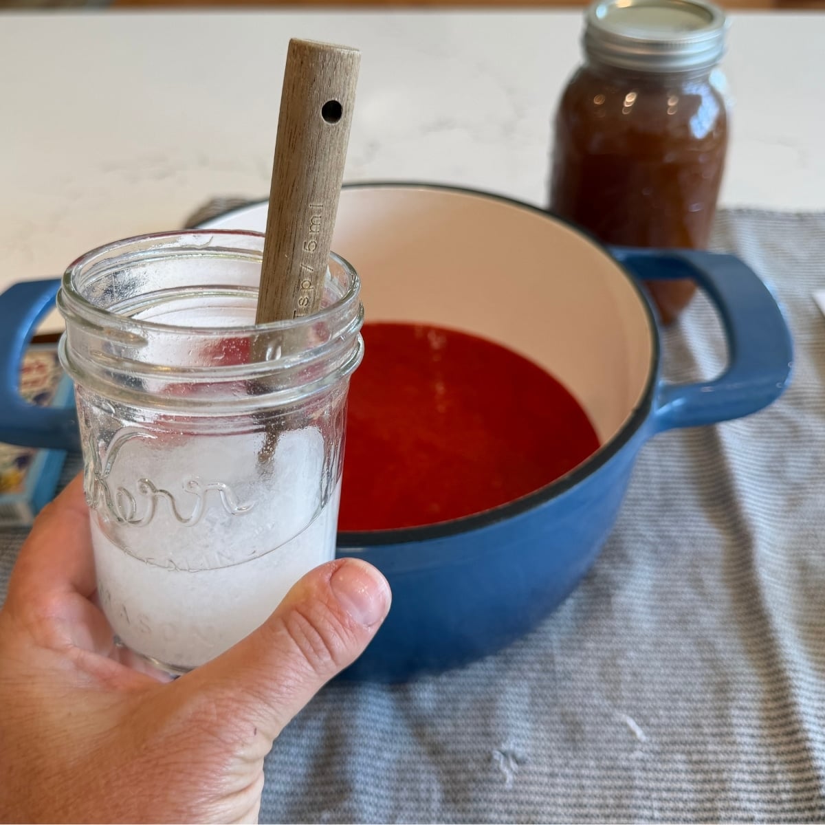 calcium water mixed in a half pint jar with strawberry puree in a blue pot in the background and a jar of honey