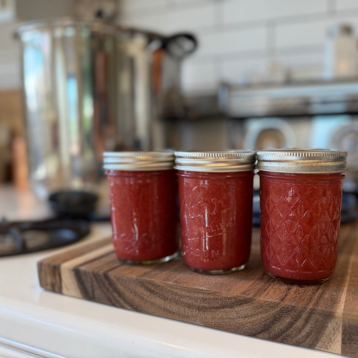 jars filled with low sygar strawberry jam canning reicpe - lids and bands on and the water bath canner or large stock pot in background on stove top