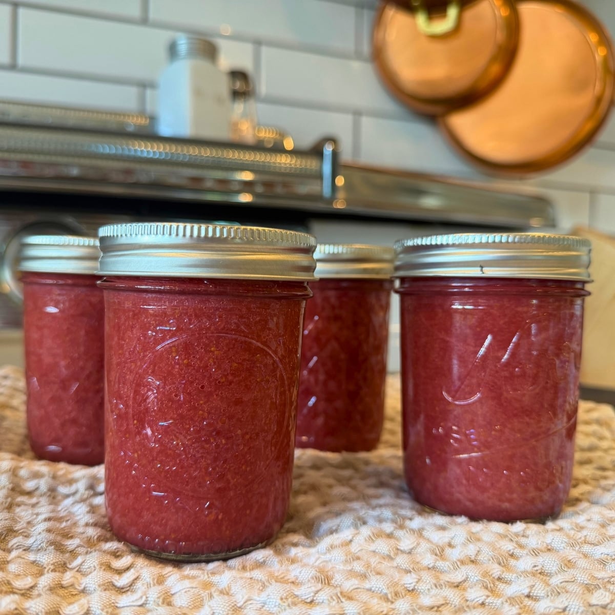 processed jars of canned strawberry jam in pint jars sitting on a clean washcloth to absorb water while they cool