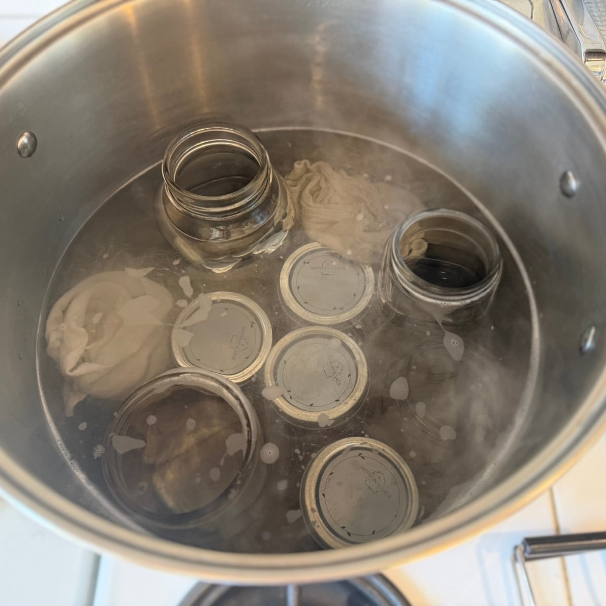 straberry jam jars in water bath canner with extra empty jars and towels to hold jam jars upright during processing time
