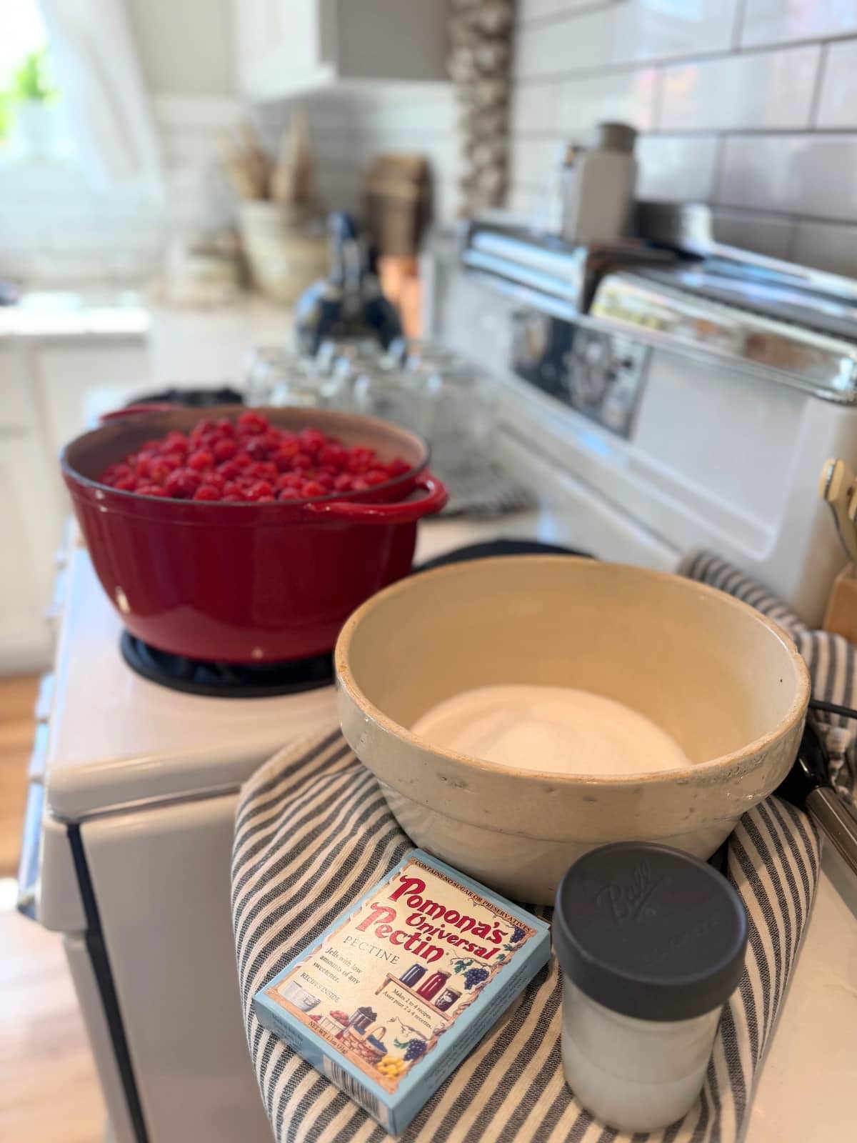 Ingreidnets for this tripple batch of raspberry jam: 12 cups of raspberries in dutch oven on stove, 3 cups of sugar with pectin in it, box of pomonas pectin and jar of calcium water with te immersion belnder on the side and clean jars on the stove