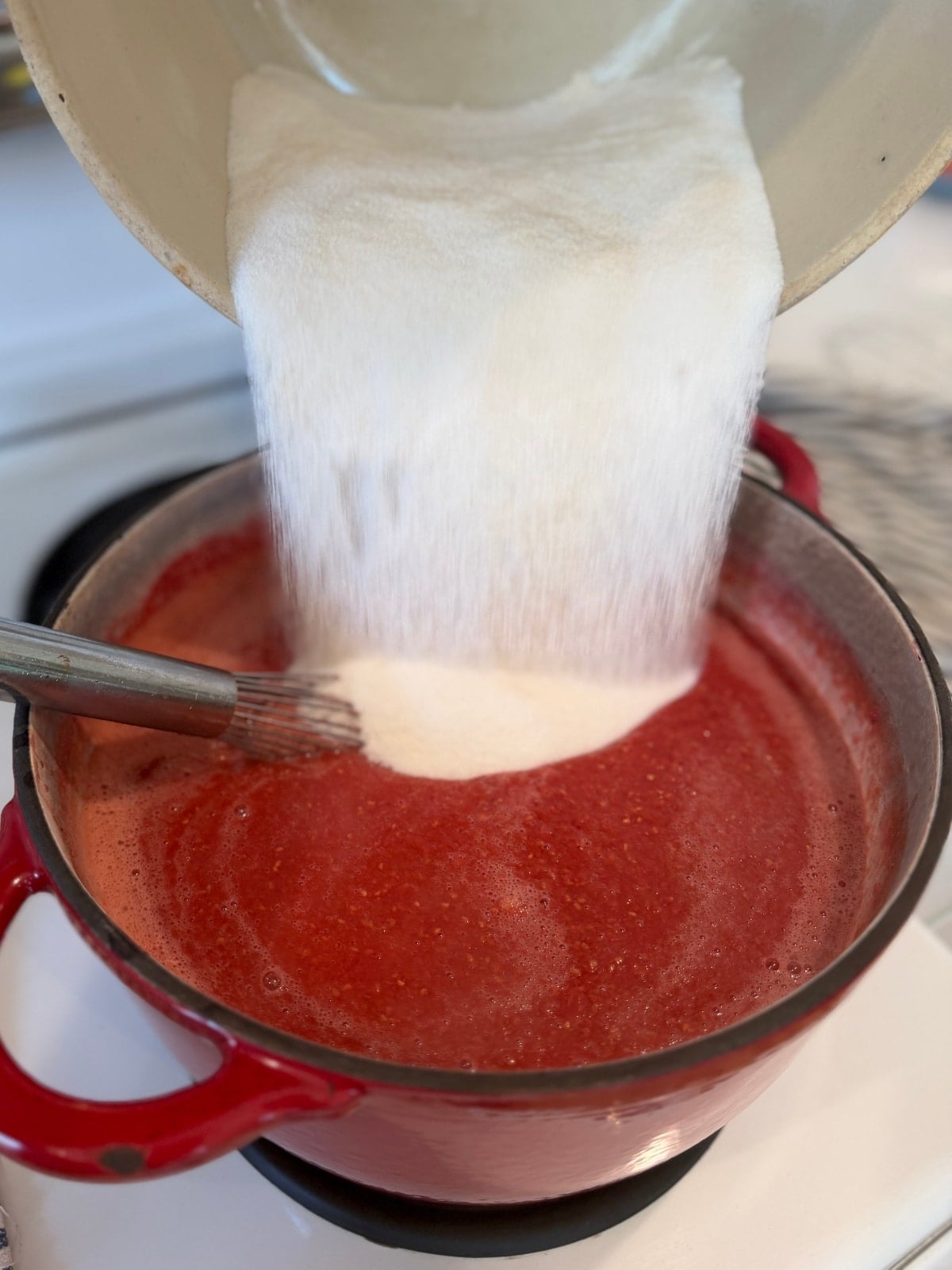 adding sugar - pectin mixture to the mashed hot pot of raspberries and calcium water